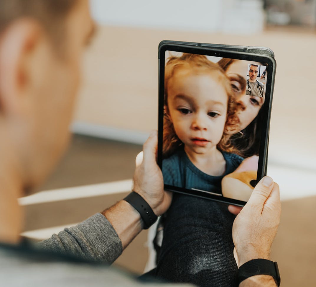 Doctor holds an iPad showing virutal visit with a child and caregiver