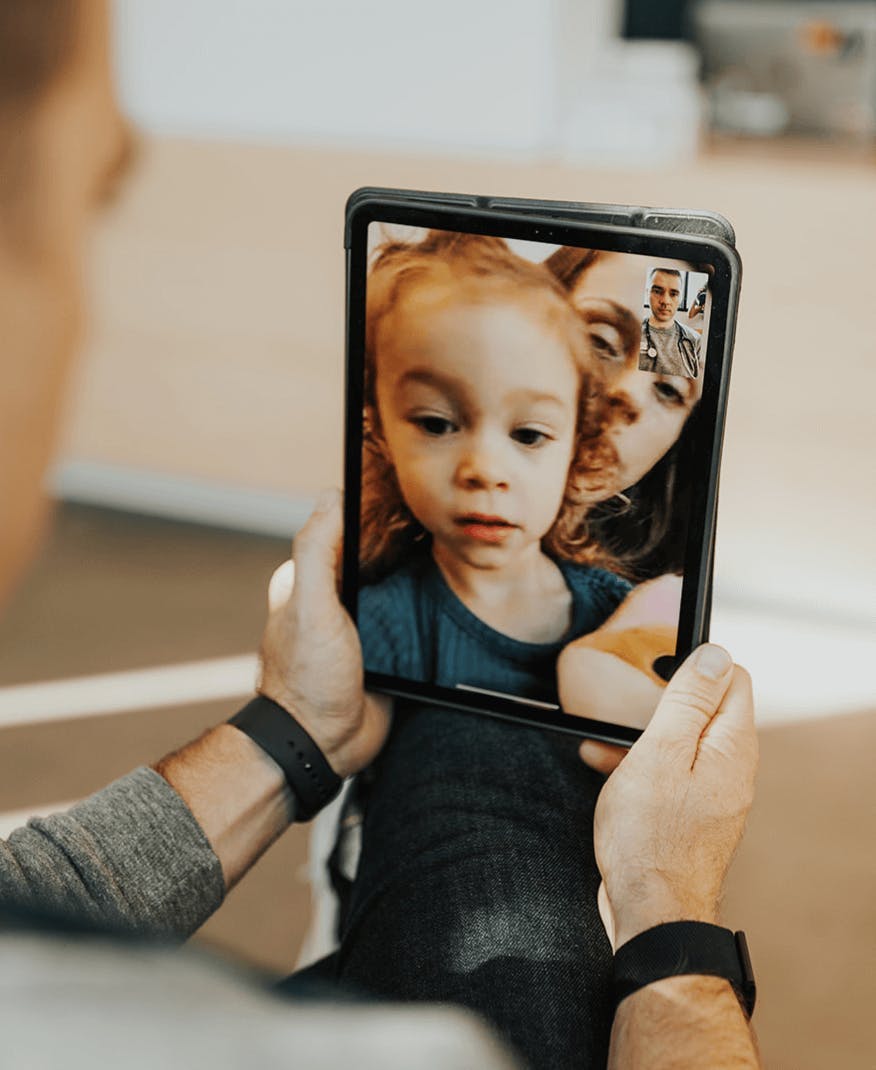 Doctor holds an iPad showing virtual visit with a child and caregiver