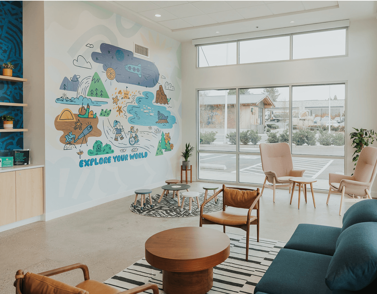 Photograph of a bright waiting room at Brave Care displaying large windows, comfortable furniture, kids area, and a mural