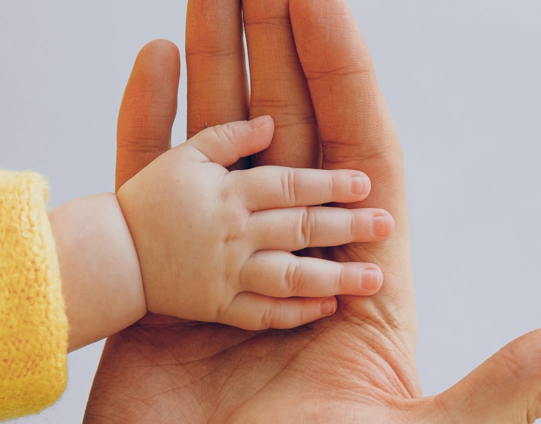 Adult hand holding a baby’s hand